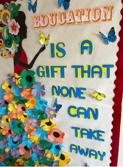 Photo of a bulletin board at Pathlight, Belmopan, which has been decorated with colored letters that spell out the saying 'Education is a gift that none can take away' and with paper flowers and the silouette of a girl.