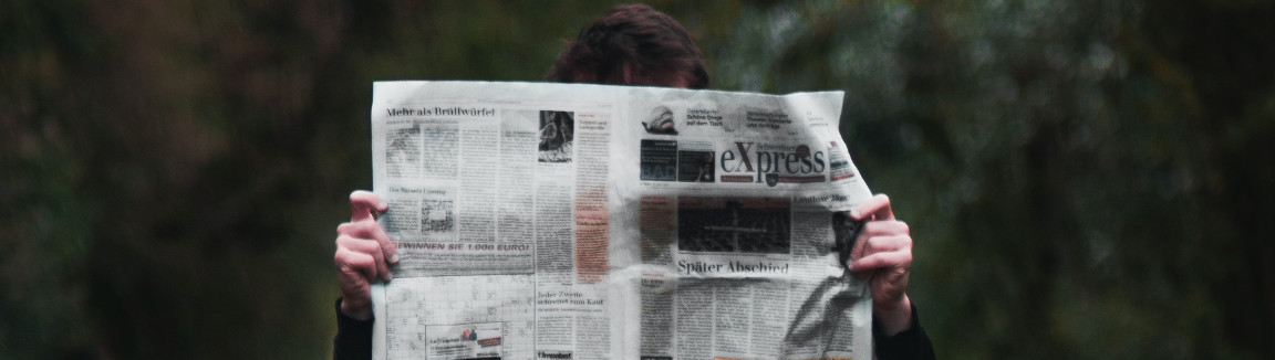 Photo of a person reading a newspaper. Superimposed on a blurred forest background.